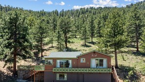 A cabin with a porch, a staircase, and a view of a forested hillside.