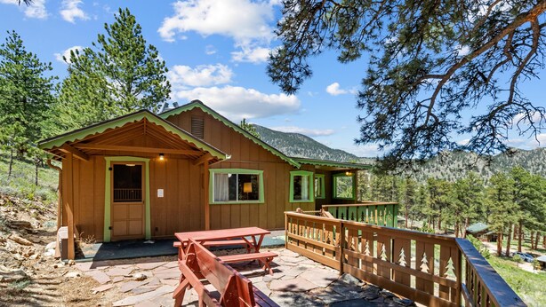 A wooden cabin with a stone patio, picnic tables, and a wooden deck.