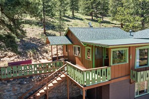 A wooden cabin with a balcony, a stone staircase, and a forested backdrop.