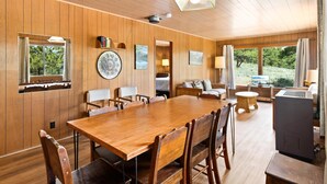A wooden-paneled room with a large dining table, chairs, a sofa, a small round table, and a TV.