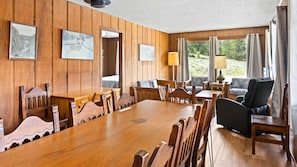 A wooden-paneled room with a dining table, chairs, a sofa, and a window with curtains.