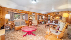 Een gezellig chaletinterieur met houten wanden, een ronde rode tafel en diverse zitmogelijkheden, zoals banken en stoelen.