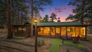 Een lodge met een groen dak, houten gevel en een eethoek met rode Adirondack stoelen.