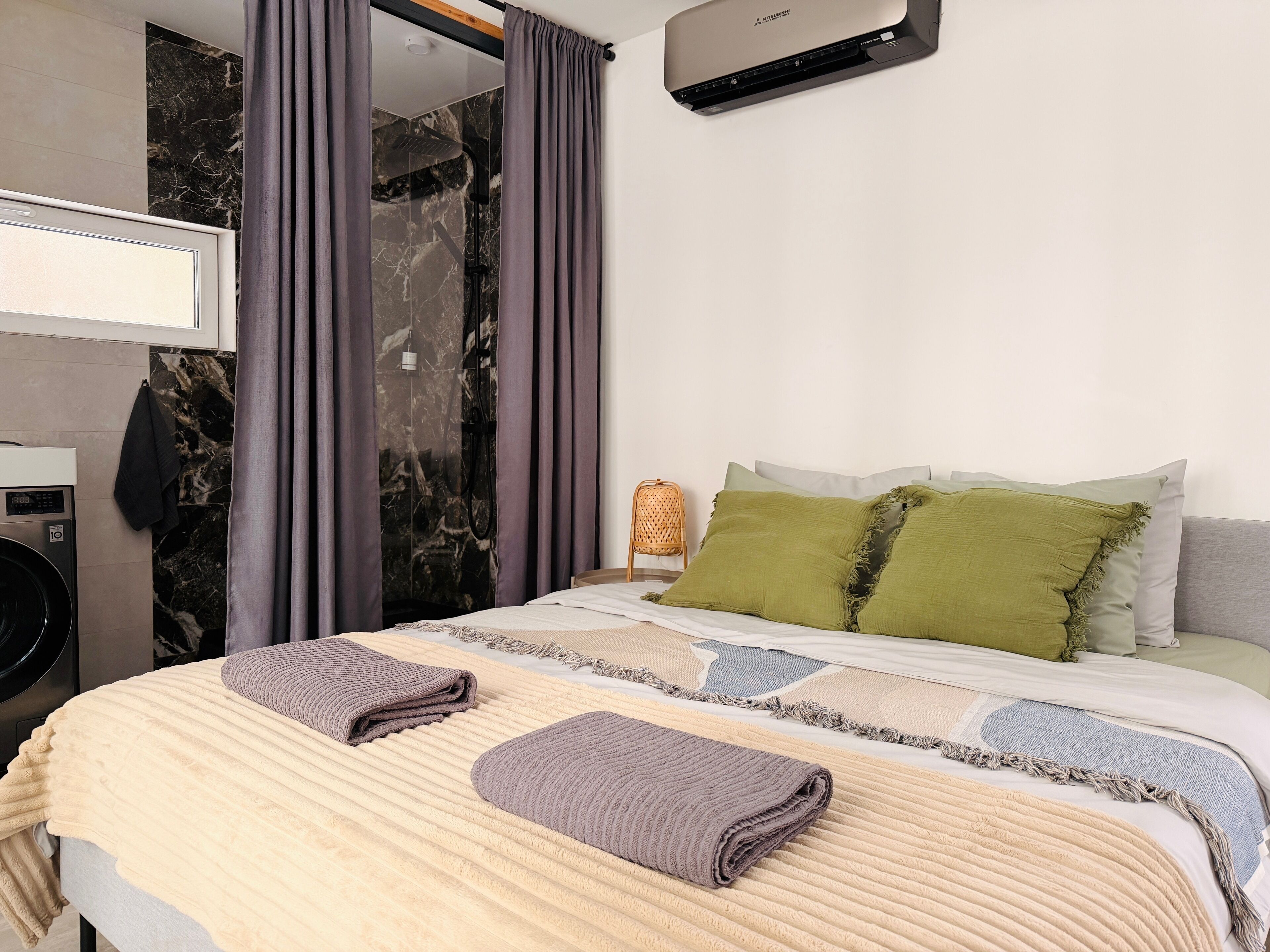 A modern bedroom with a bed, a washing machine, and a shower area.