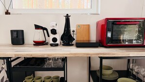 A kitchen counter with a coffee maker, a red microwave, a wooden cutting board, and a black spatula.