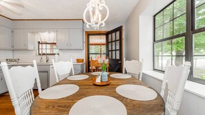 A dining area with a wooden table, white chairs, and a chandelier. - Smoky Mountain Hideaway | Spacious Yard & Firepit (Maryville)