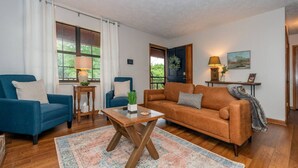 A living room with a blue armchair, a brown sofa, a coffee table, and a rug. - Smoky Mountain Hideaway | Spacious Yard & Firepit (Maryville)