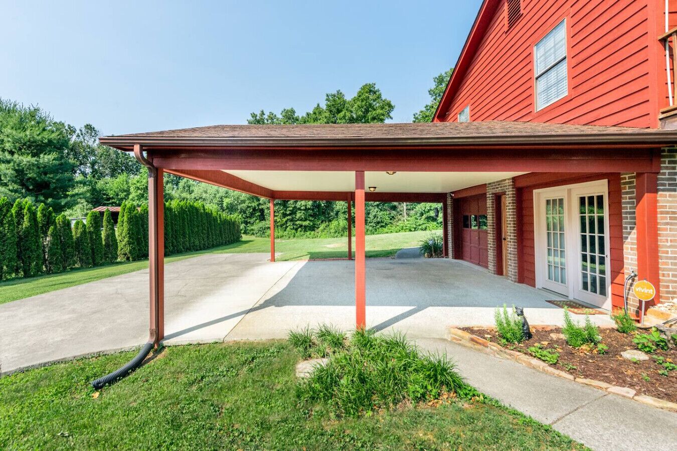 Ein überdachter Patio-Bereich mit Betonboden, umgeben von einer Ziegelmauer und einem roten Gebäude.