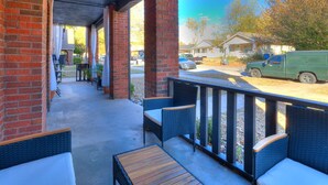 A covered outdoor seating area with brick walls, wicker furniture, and a view of a street with parked vehicles. - Rockford`s hidden gem (Tulsa)