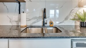 A kitchen with a stainless steel sink, marble backsplash, wooden shelves, and a potted plant. - Rockford`s hidden gem (Tulsa)