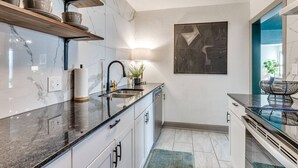A modern kitchen with marble countertops, a built-in dishwasher, and a large window with a view. - Rockford`s hidden gem (Tulsa)