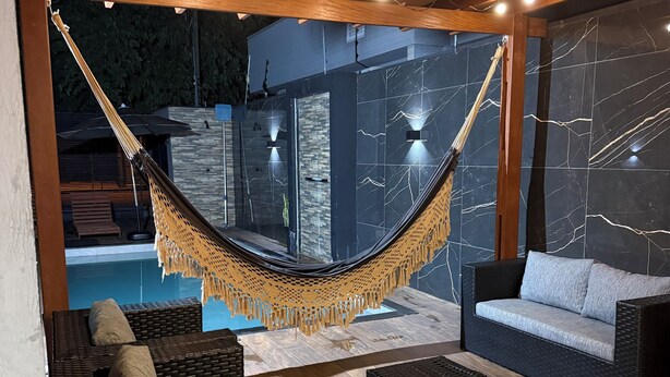 Uma rede pendurada sobre uma área de piscina, com assentos externos e vista para a piscina.