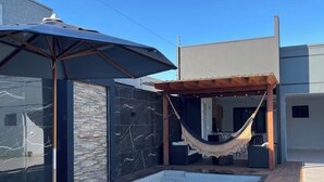 Piscina com rede e guarda-sol, cercada por arquitetura moderna.
