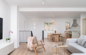 Ein geräumiger Wohnbereich mit einer Couch, einem Esstisch mit Stühlen, einem kleinen Beistelltisch und einem an der Wand montierten Fernseher.