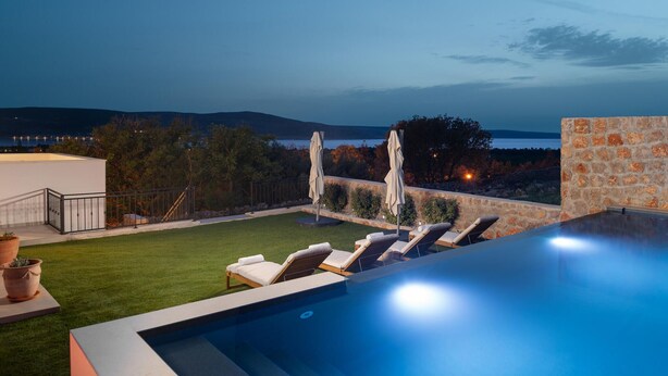 An infinity pool with lounge chairs and umbrellas, a stone wall, and a view of the sea and hills. - Beautiful home in Seline (Seline)