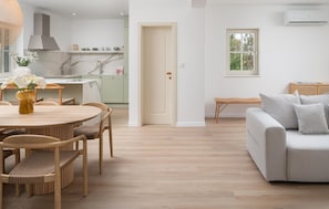 Ein modernes Wohnzimmer mit einem grauen Sofa, einem Esstisch mit Stühlen und einer Küche im Hintergrund.