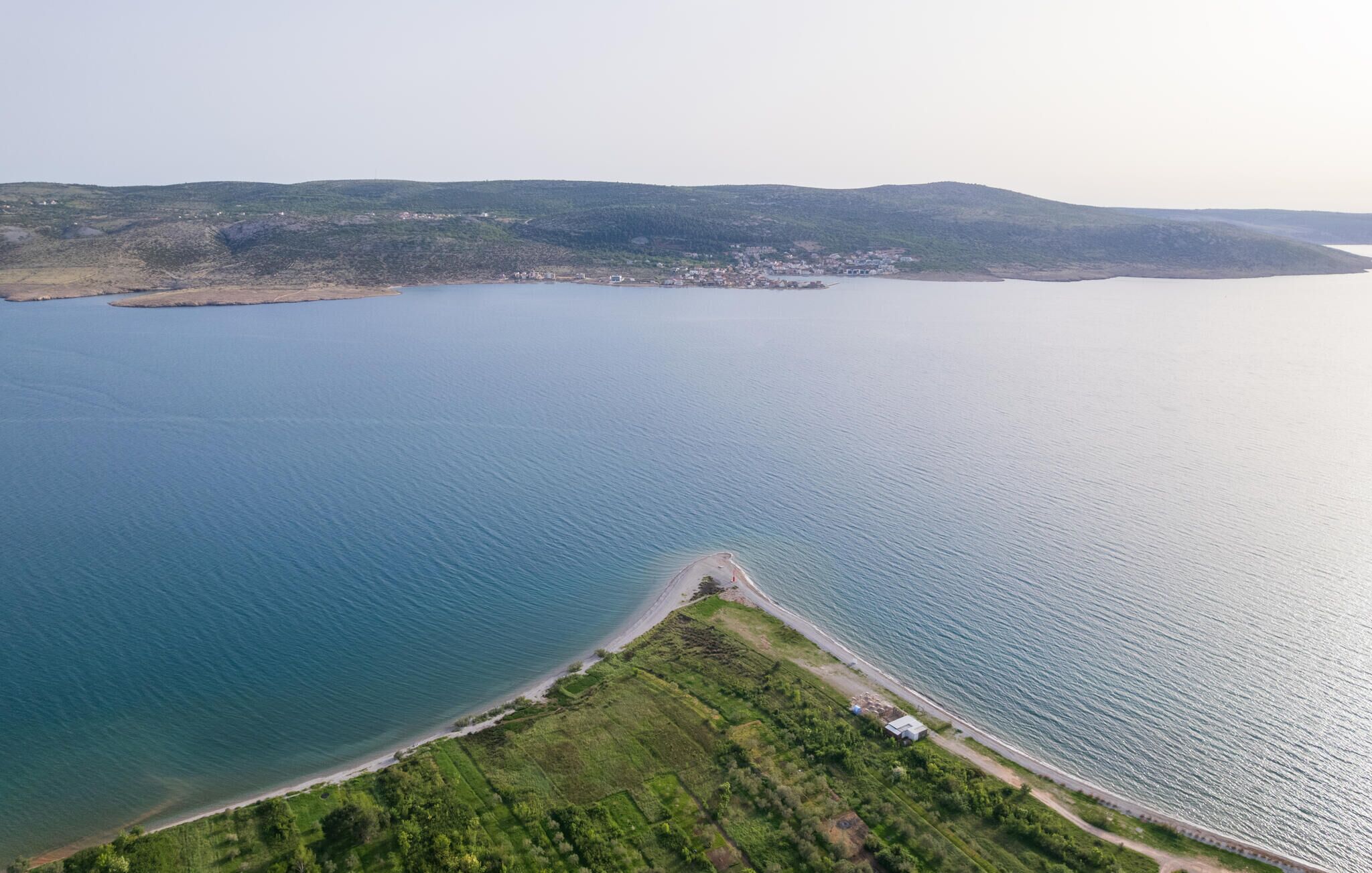 Oversigtsbillede af et kystområde med strand, grønne marker og en lille bebyggelse.