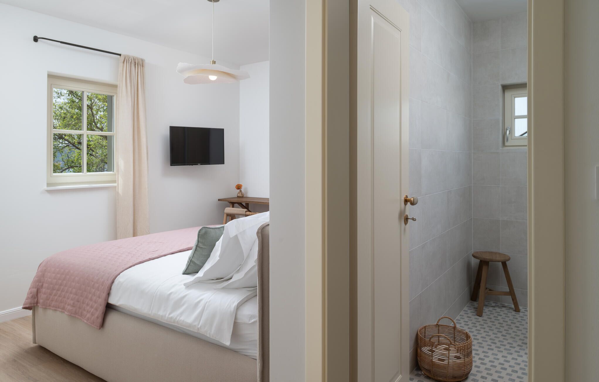 Une chambre à coucher comprenant un lit, une télévision, une fenêtre et une salle de bain avec une douche et un tabouret.