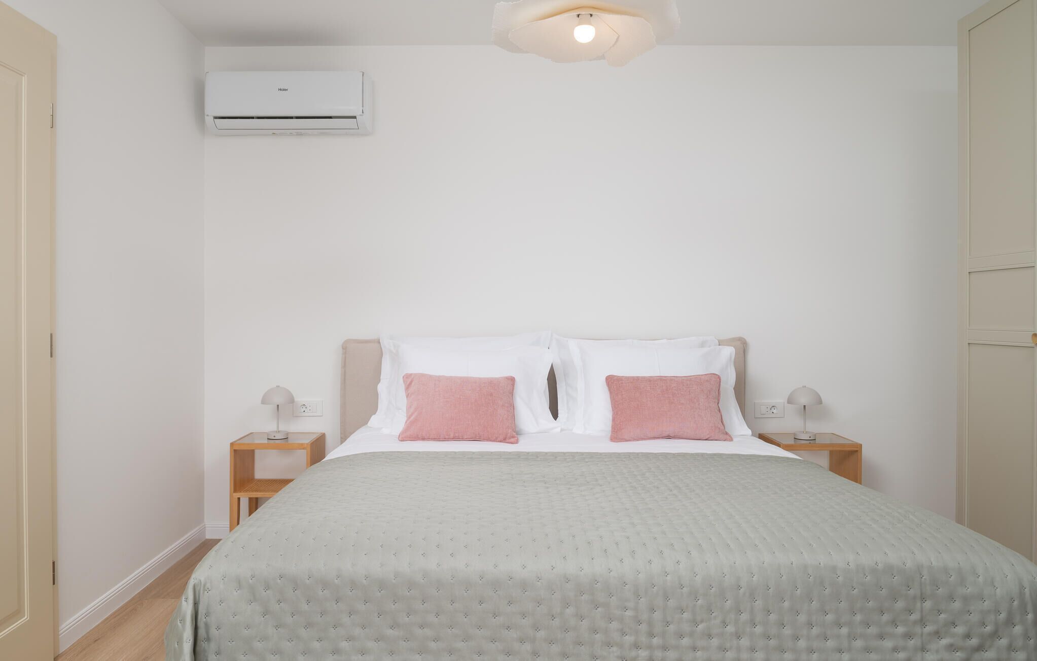 A bedroom with a bed, two bedside tables, a nightstand, an air conditioning unit, and a wall-mounted light fixture.