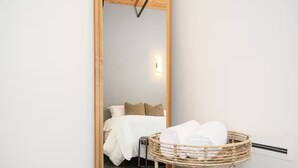 Een hotelkamer met een grote spiegel, een bed met wit beddengoed, een klein nachtkastje en een rieten mand met handdoeken.
