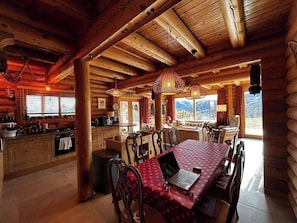 L’intérieur d’une cabane en rondins comprend un coin repas, une cuisine et de grandes fenêtres offrant une vue sur les montagnes.