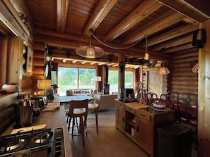 L’intérieur d’un chalet rustique comprend une cuisine, un coin repas et une grande fenêtre donnant sur le paysage extérieur.