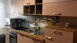 A modern kitchen with pink cabinets, a wooden countertop, stainless steel appliances, and a backsplash with a distressed finish.