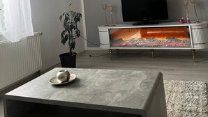 A living room with a flat-screen TV on a white cabinet, a potted plant, and a small table with a decorative item.