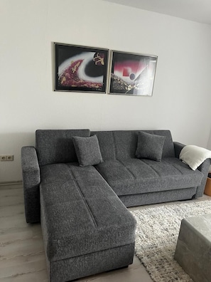 Ein modernes Wohnzimmer mit einem grauen Ecksofa, einem weißen Teppich und zwei abstrakten Bildern an der Wand.