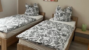 A bedroom with two single beds, a wooden headboard, a nightstand, a green vase, and a floral painting on the wall.