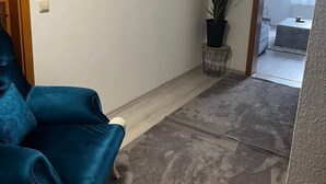 A living room with a blue sofa, a framed painting on the wall, and a potted plant.