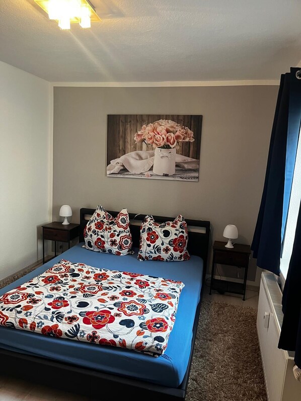 Une chambre à coucher comprenant un lit, deux tables de chevet, une commode, un radiateur et un tableau accroché au mur.