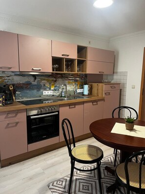 Eine moderne Küche mit rosa Schränken, einer großen Kochinsel mit Spüle und einem Essbereich mit rundem Tisch und Stühlen.