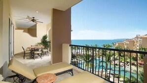 A balcony with a pool view, a ceiling fan, and a dining area with chairs and a table. - Beachfront 1BR Suite at Villa del Palmar Flamingos - Pools, Spa & Sunsets (Nuevo Vallarta)