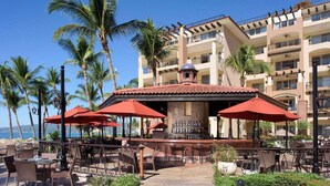 A beachfront bar with outdoor seating, palm trees, and a view of the ocean. - Beachfront 1BR Suite at Villa del Palmar Flamingos - Pools, Spa & Sunsets (Nuevo Vallarta)