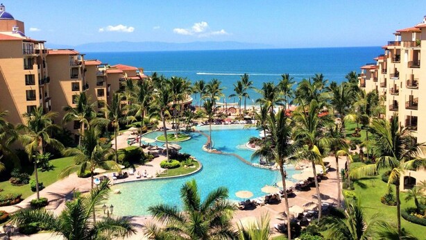 A resort with a central swimming pool, palm trees, and ocean views. - Beachfront 1BR Suite at Villa del Palmar Flamingos - Pools, Spa & Sunsets (Nuevo Vallarta)