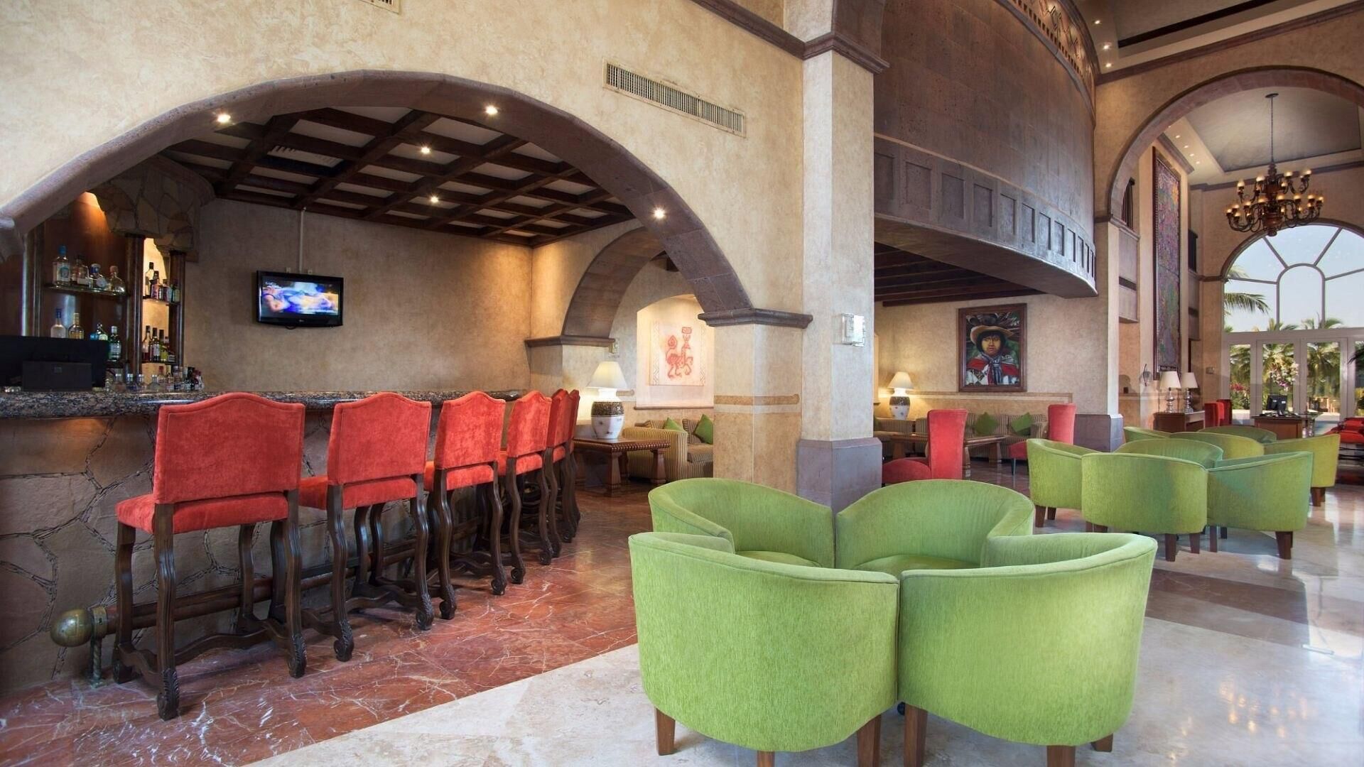 A lobby with a bar area, red and green chairs, and a television screen.