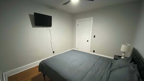 Une chambre à coucher comprenant un lit, un téléviseur fixé au mur, un ventilateur de plafond et une table de chevet avec une lampe.