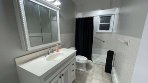 Une salle de bain avec un meuble-lavabo blanc, un miroir, des toilettes et un espace douche.