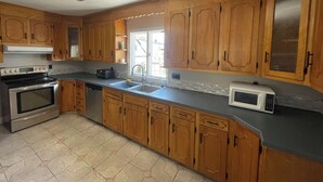 Une cuisine avec des meubles de rangement en bois, une cuisinière, un four à micro-ondes et un ventilateur de plafond.