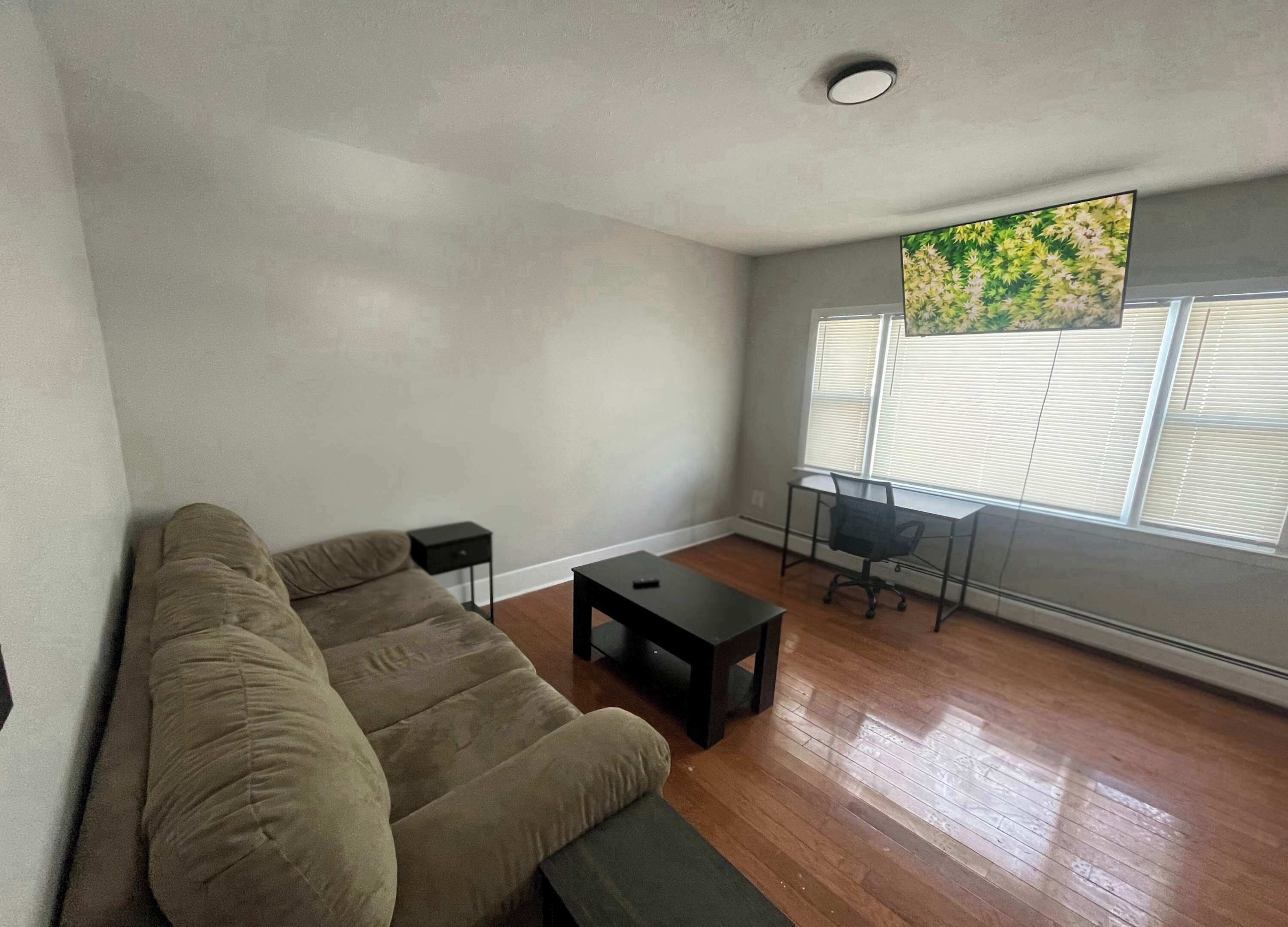A living room with a sofa, a small table, a chair, and a window with blinds.