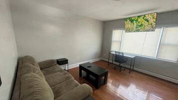 A living room with a sofa, a small table, a chair, and a window with blinds.