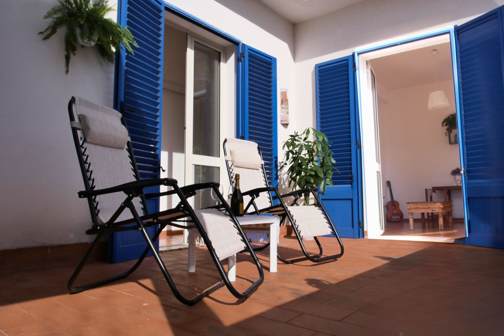 A terrace with two lounge chairs, a table, and a potted plant.