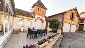 Un patio con una mesa y sillas para comer, un edificio de ladrillo con una torre, y un muro de piedra con macetas.