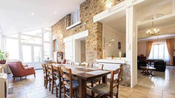 Un comedor amplio con una larga mesa de madera y sillas, una pared de piedra y vistas de la habitación contigua.