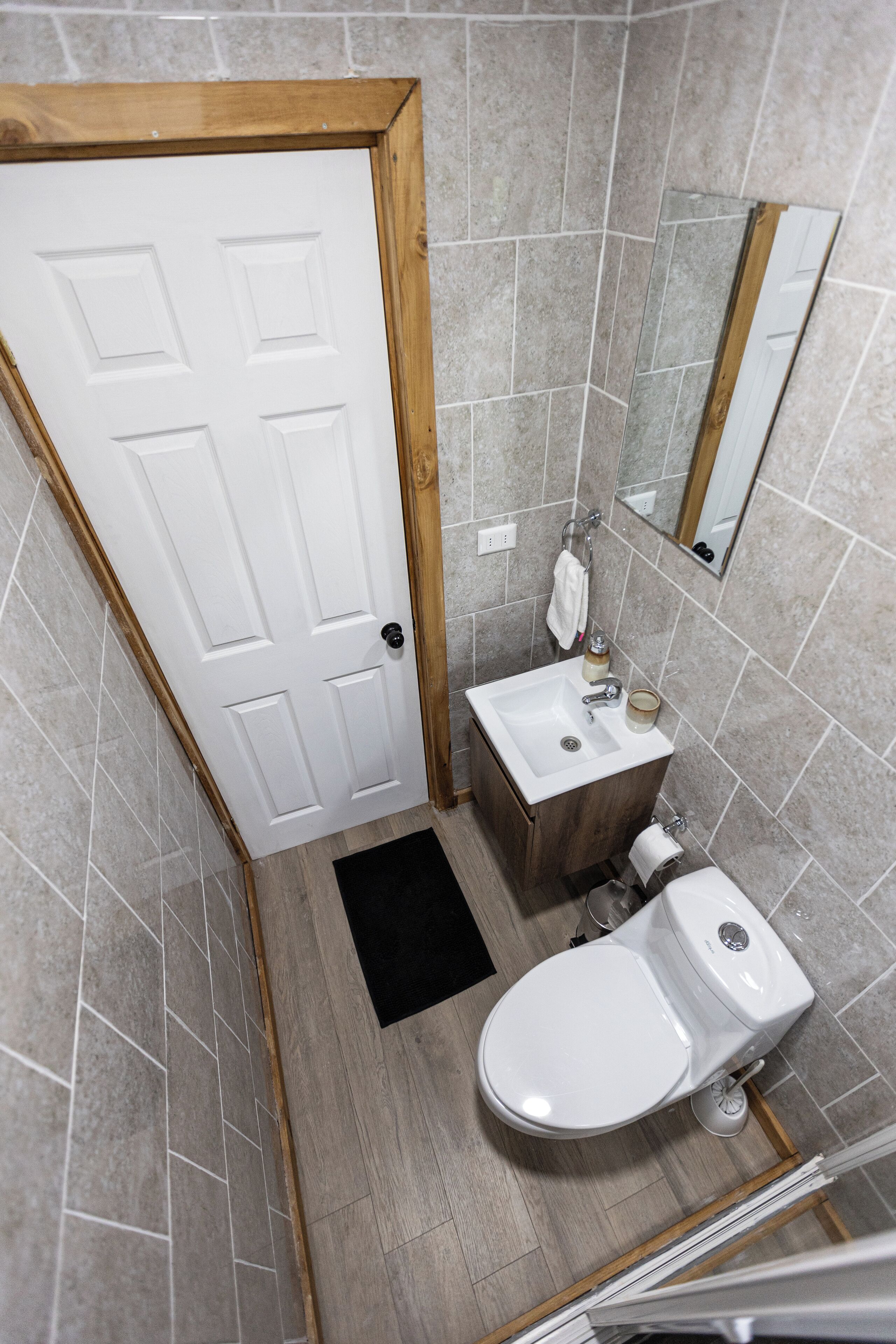 A bathroom with a white door, a sink, a toilet, and a mirror.