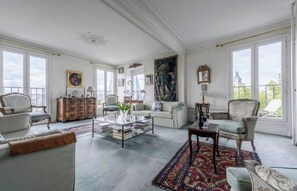 Ein geräumiges Wohnzimmer mit großem Fenster, Couchtisch, Sofas und einem gemusterten Teppich.