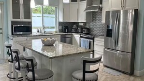 A modern kitchen with a central island, stainless steel appliances, and white cabinetry. - Villa Nueva (Key Largo)