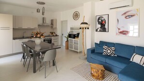 Une cuisine moderne avec des meubles blancs, une table à manger avec des chaises, un canapé bleu et une machine à café.