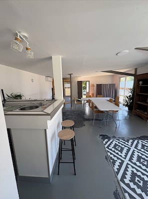 Et moderne køkken med en central ø, barstole, et spiseområde med bord og stole, og en gulvtæppe med et mønster.